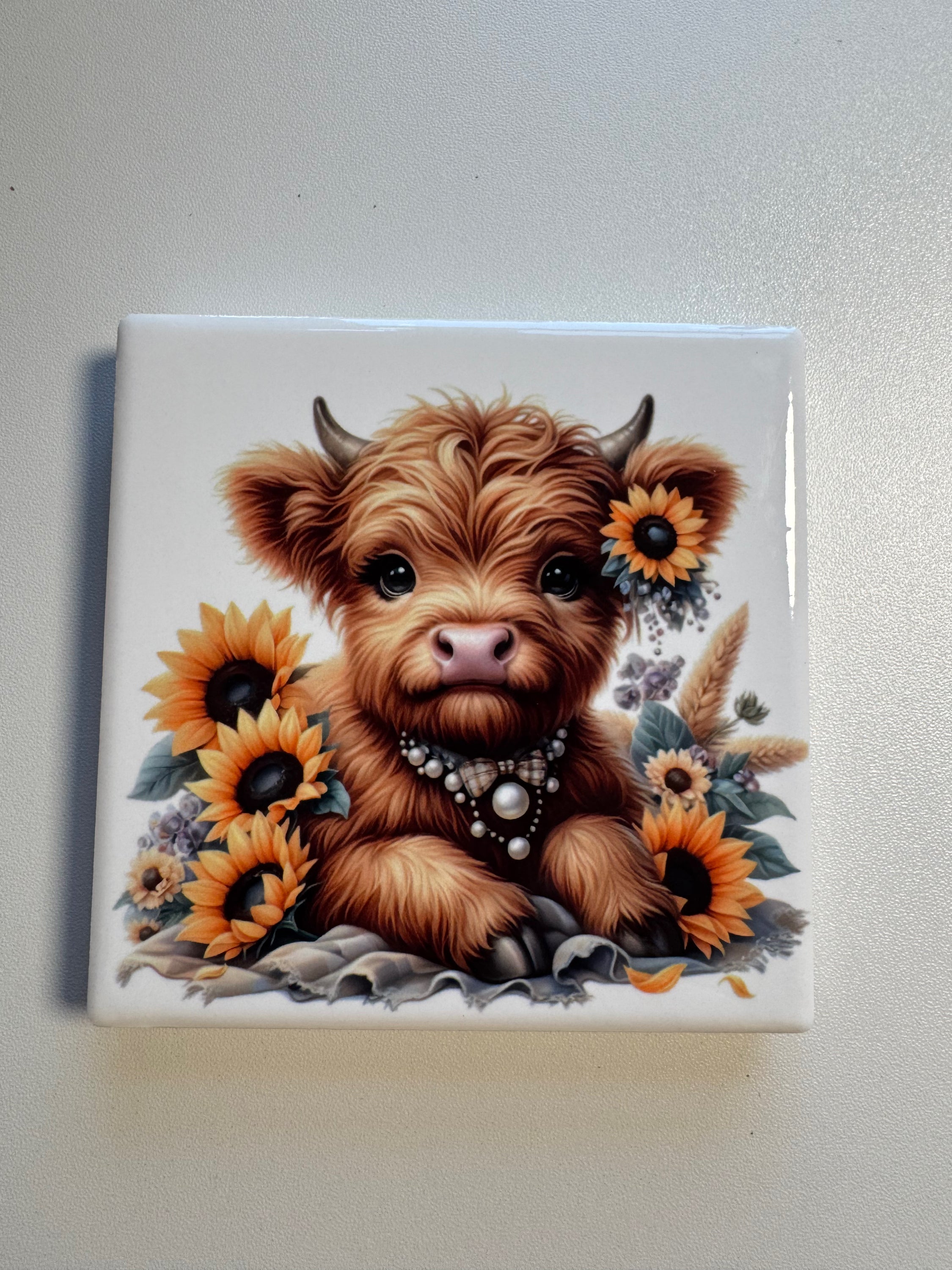 Ceramic tile with a design of a Highland cow surrounded by sunflowers and flowers.